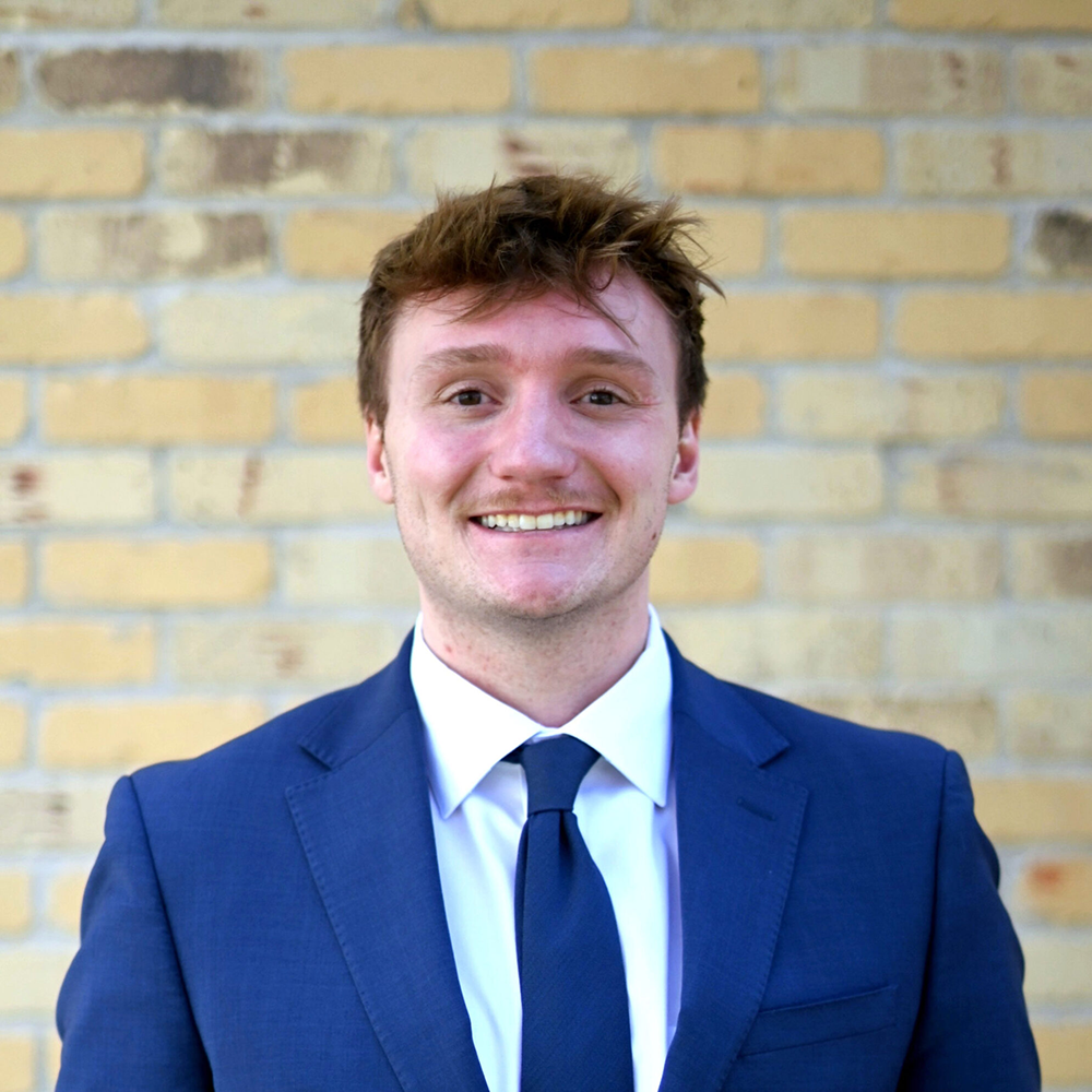 new - Kittelsen Law | Law Firm in Monroe providing legal services Smiling man in a blue suit and tie posing against a yellow brick wall.